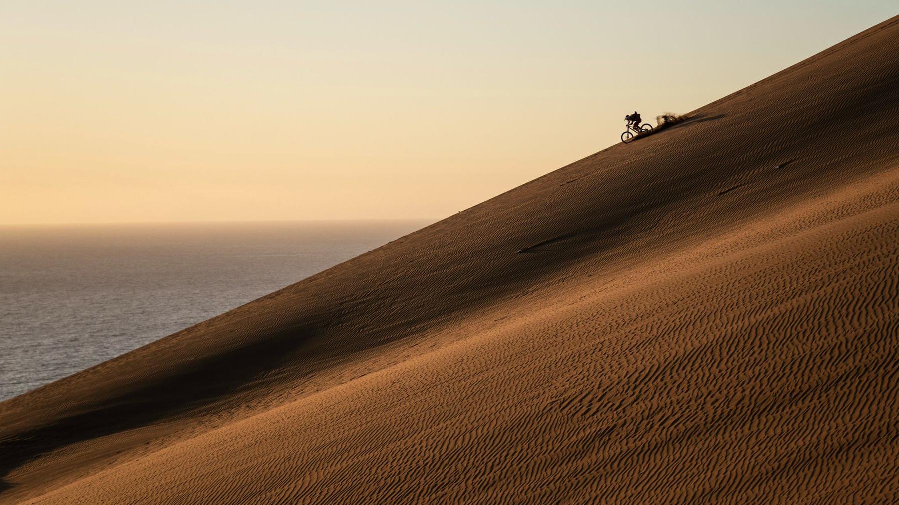 Ciclista descendiendo una duna al atardecer